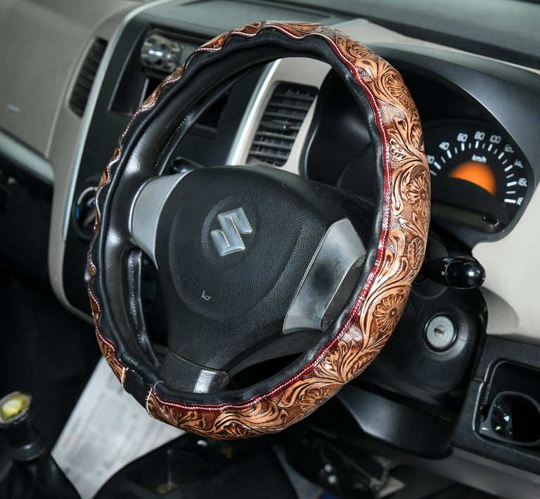 Brown embossed floral leather steering wheel cover on a black Suzuki car interior.