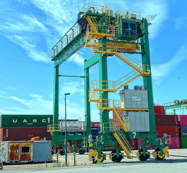 A green and yellow rubber-tired gantry crane standing over shipping containers at a busy marine terminal.