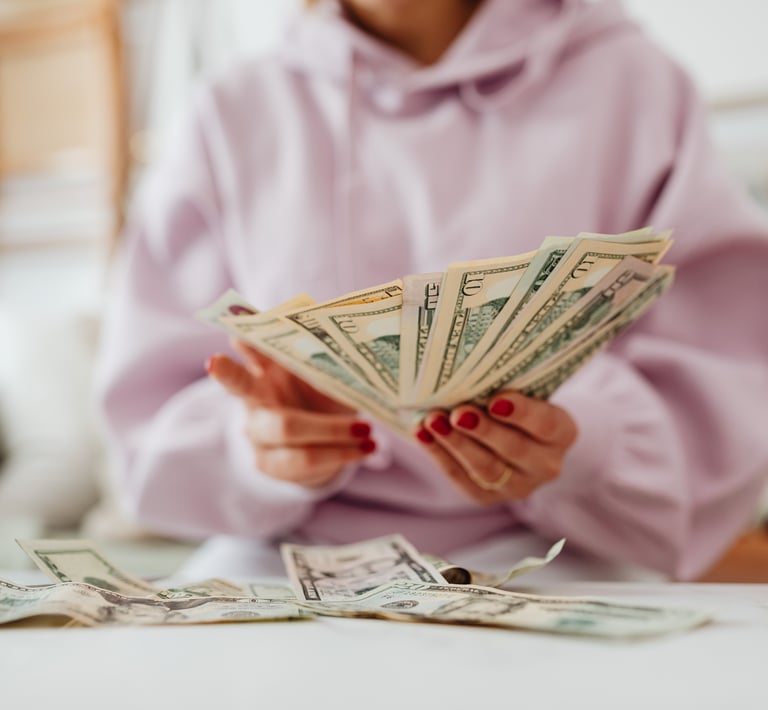 A woman in a pink hoodie, sitting at a tble and counting money.