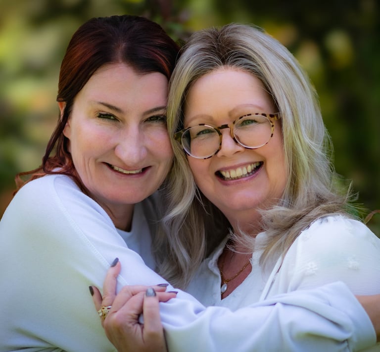 Two happy women in white shirts smiling and hugging outdoors with a soft blurred background. Athens