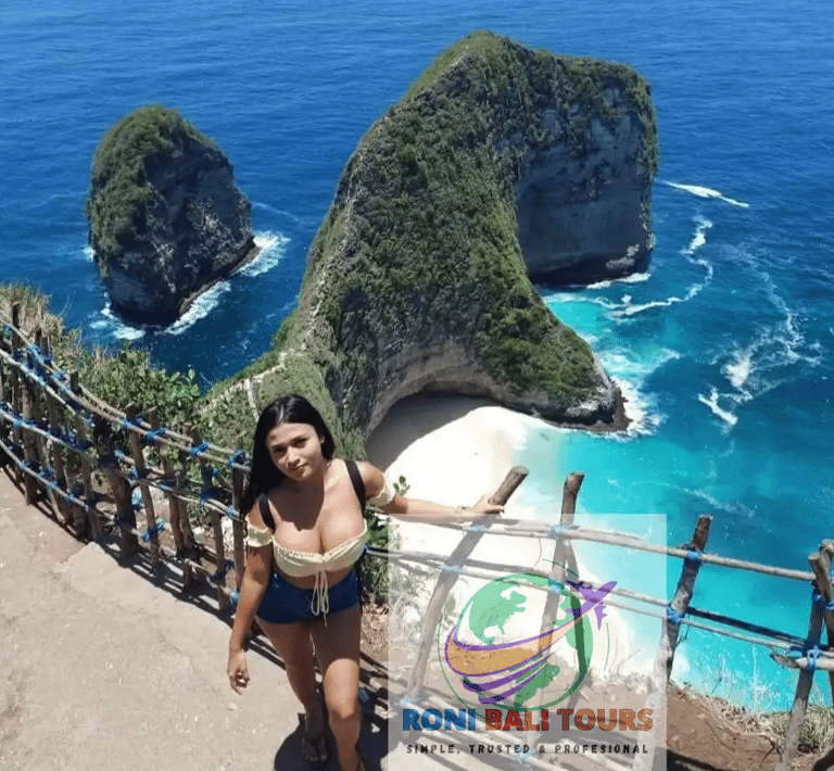 A woman stands overlooking Kelingking Beach in Nusa Penida, Bali with views of the iconic T-Rex cliff and turquoise water.