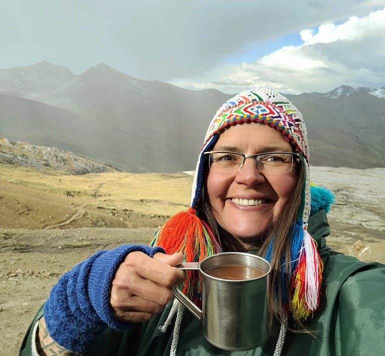 Smiling woman in a colorful hat holding a metal mug during a mountain hike.