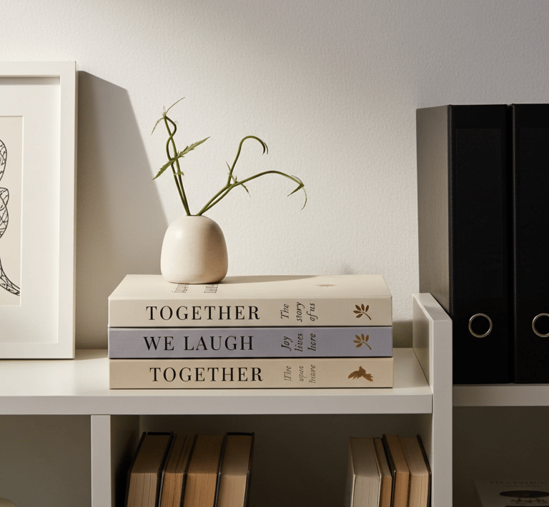 Stack of decorative books with minimalist gold foil accents styled on a bookshelf with a vase