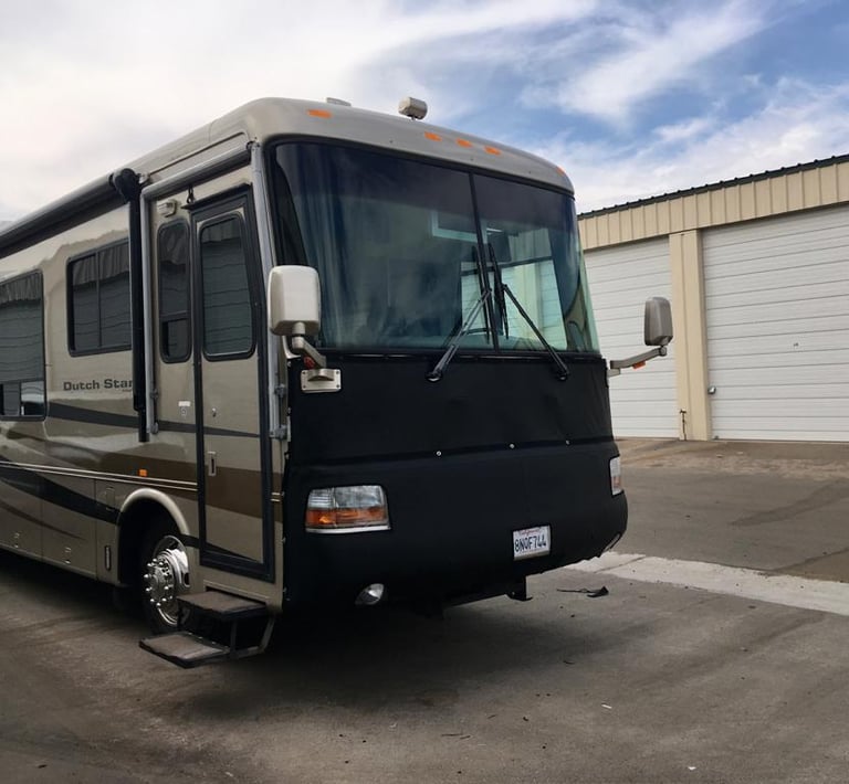 A luxury Newmar Dutch Star motorhome RV parked at a storage facility with a protective front mask cover.