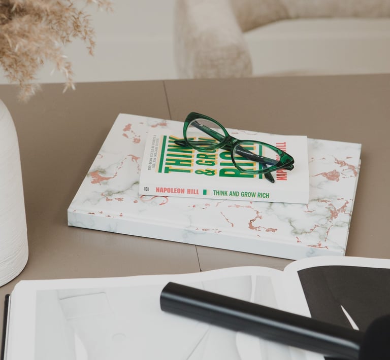 Green reading glasses on a Think and Grow Rich book over a marble notebook on a desk.