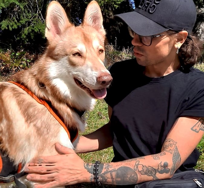 photo of a man wearing a black baseball cap and glasses sitting on the grass with a large brown dog
