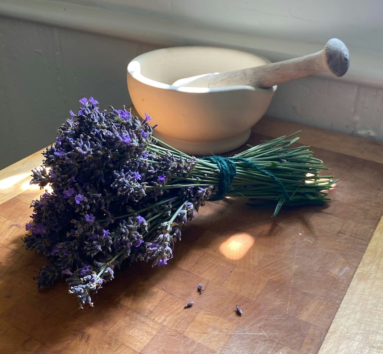 Fresh lavender bundle and a ceramic mortar and pestle on a wooden cutting board.