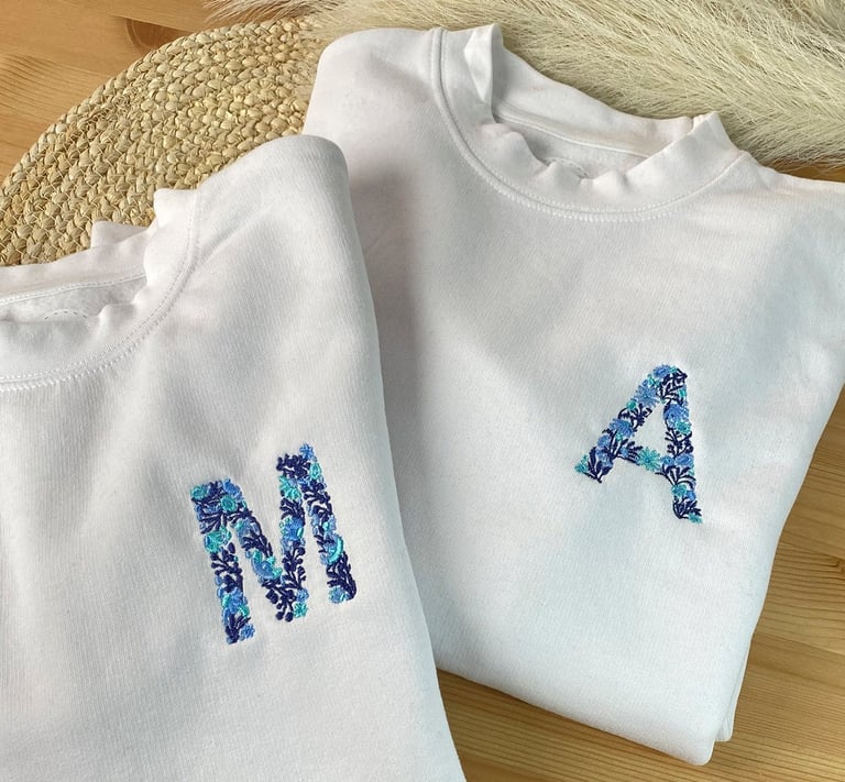 Two white custom sweatshirts with blue floral embroidery of initials M and A.