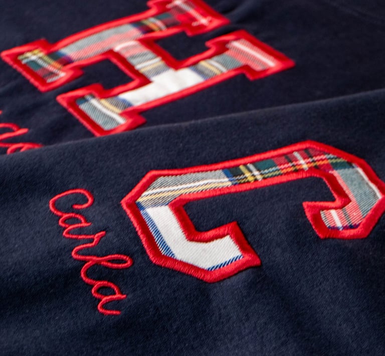 Close-up of a navy blue sweatshirt featuring red embroidered letters with plaid fabric inlay.