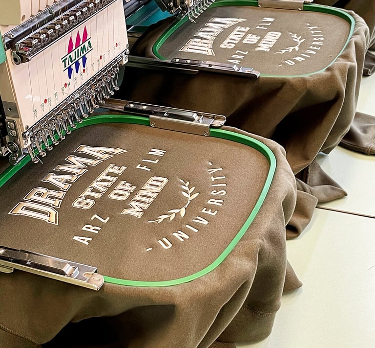 Tajima commercial embroidery machine stitching custom university logos on brown sweatshirts.