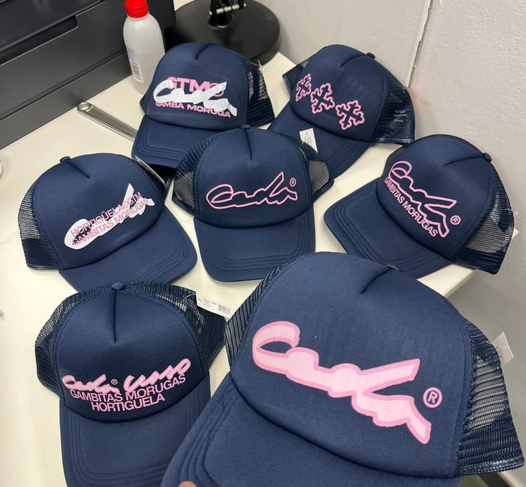 Navy blue Gambitas Morugas trucker hats featuring pink embroidered logos on a white table.