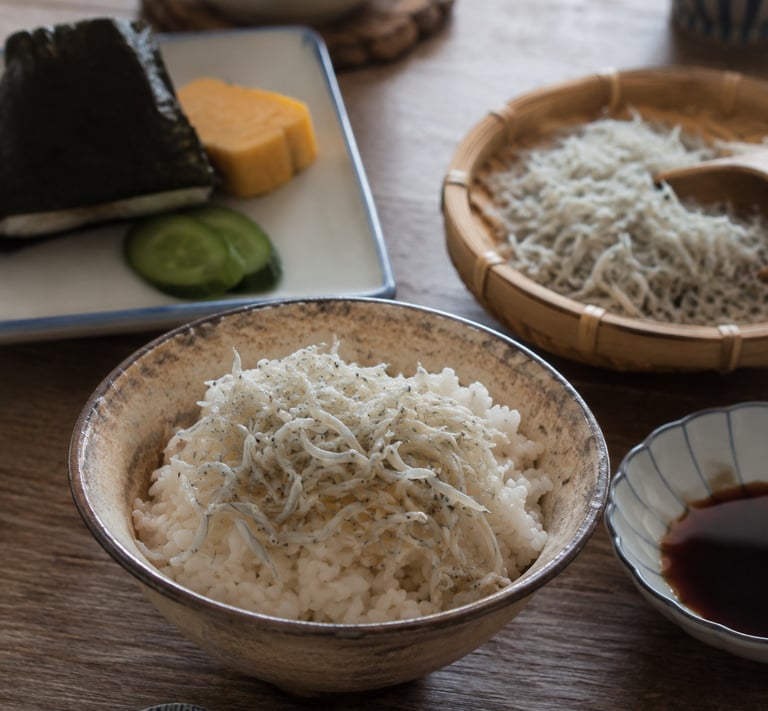 Traditional Japanese breakfast with a bowl of steamed white rice topped with whitebait shirasu and onigiri.