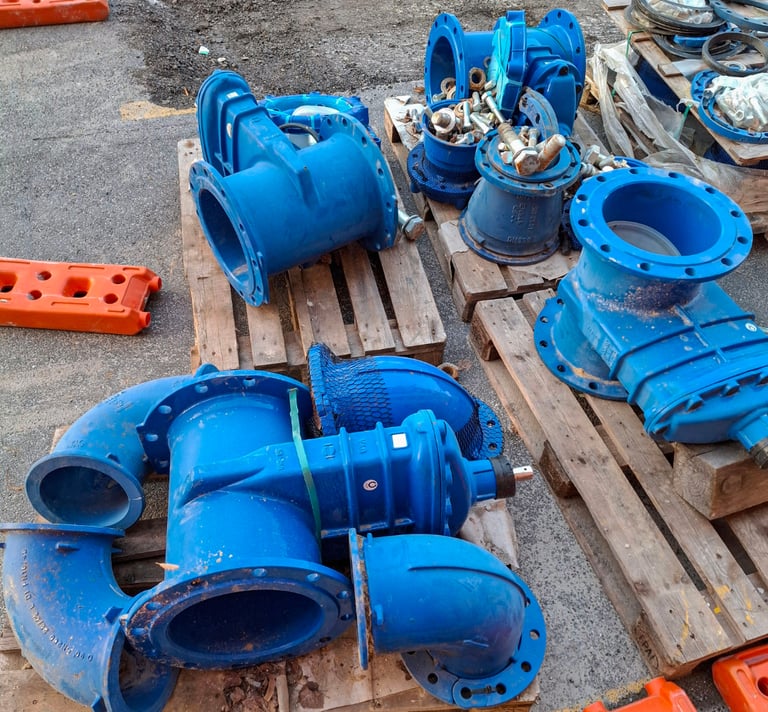 Industrial blue ductile iron flanged pipe fittings and valves on wooden pallets at a construction site.