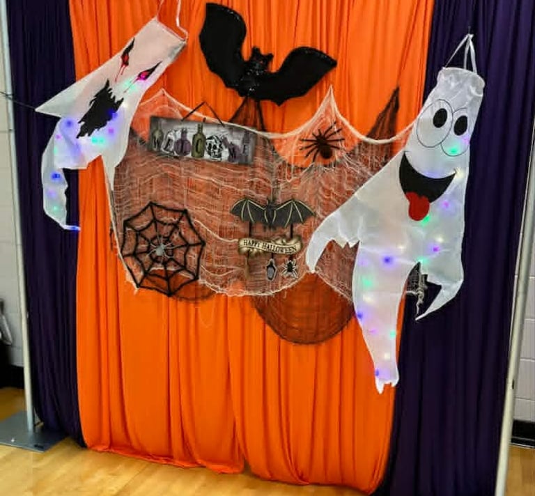 Halloween photo booth backdrop featuring orange and purple curtains with hanging ghosts and bat decorations.