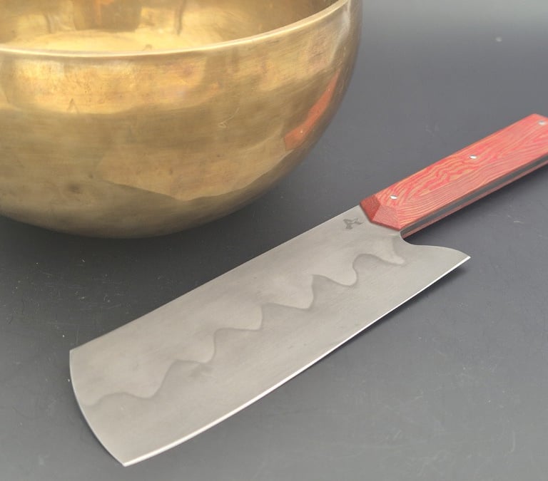 Couteau de cuisine polyvalent avec manche rouge à coté d'un bol dorée
