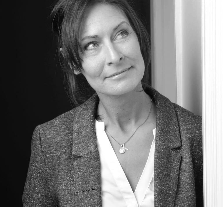 A professional black and white portrait of a woman in a grey blazer looking upwards thoughtfully.