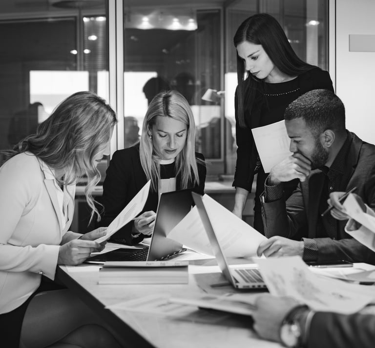 a group of people sitting around a table looking intently at paperwork and screens