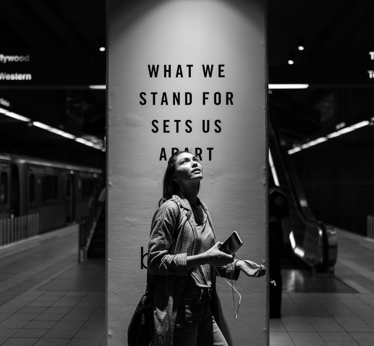 grayscale photo a woman standing in a subway station next to a social impact ad