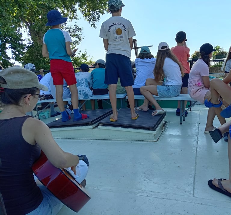 Colonie : animatrice à la guitare, jeunes réunis sur le pont.