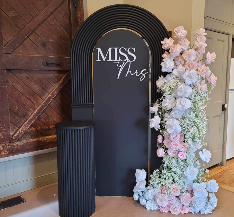 Black backdrop with a white Miss To Mrs sign and pink, white florals with baby breaths