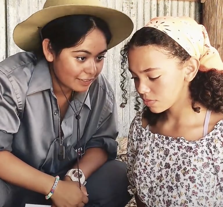a young woman in a sheriff hat speaking to and a teen girl in a head scarf