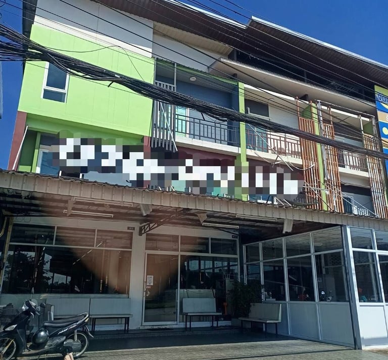 A modern three-story green and white office building with large glass windows and parked motorbikes out front.