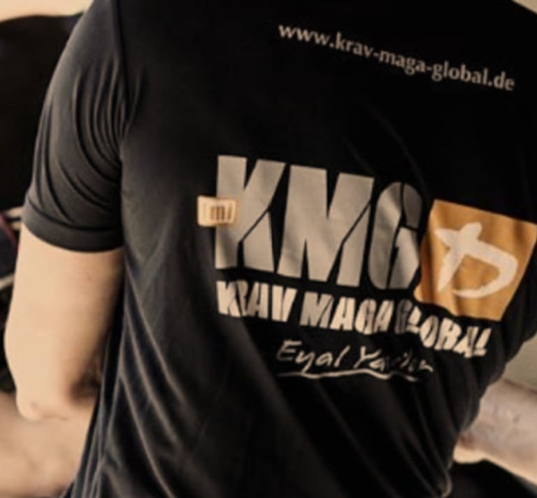 KMG Krav Maga Global instructor wearing a branded black t-shirt during a self-defense training session.