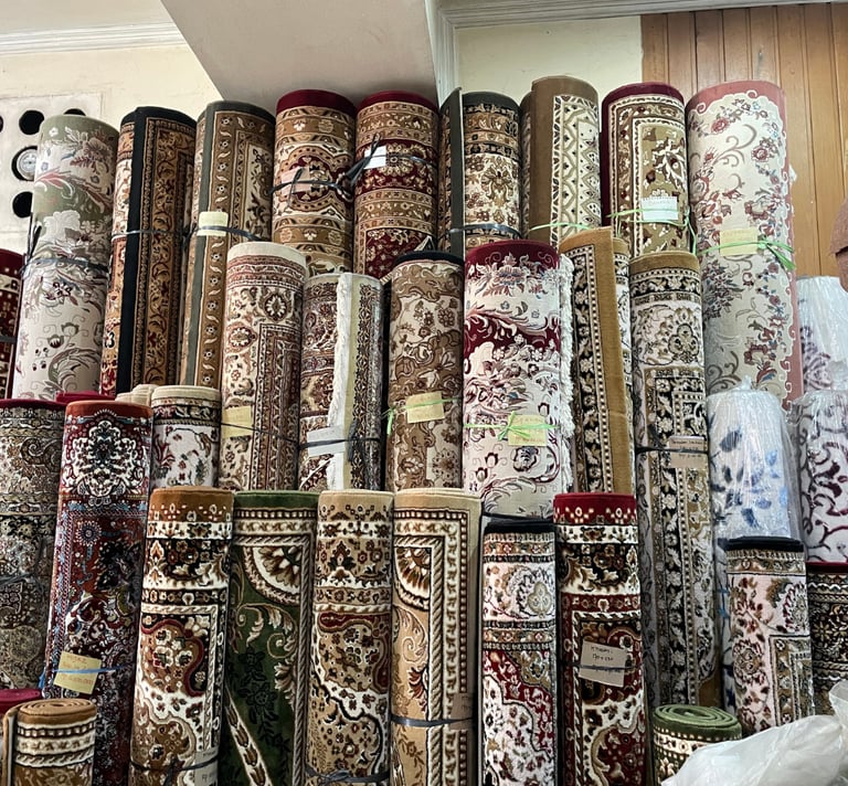 A variety of rolled oriental area rugs with intricate floral patterns displayed in a carpet shop warehouse.