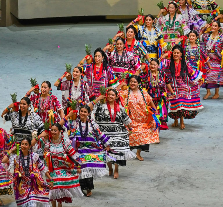 Mujeres bailando Flor de Piña con huipiles y piñas en la Guelaguetza, Oaxaca