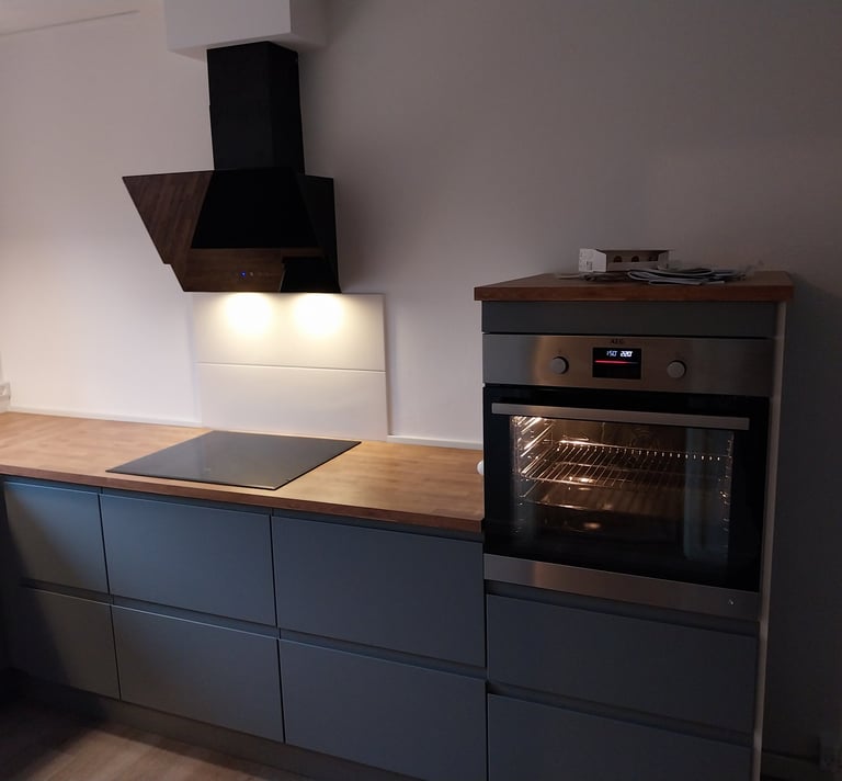 Moderne køkken med grå skabe, træbordplade, induktionskogeplade og indbygget ovn.