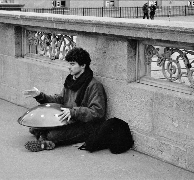 a man sitting on the sidewalk playing the handpan instrument.