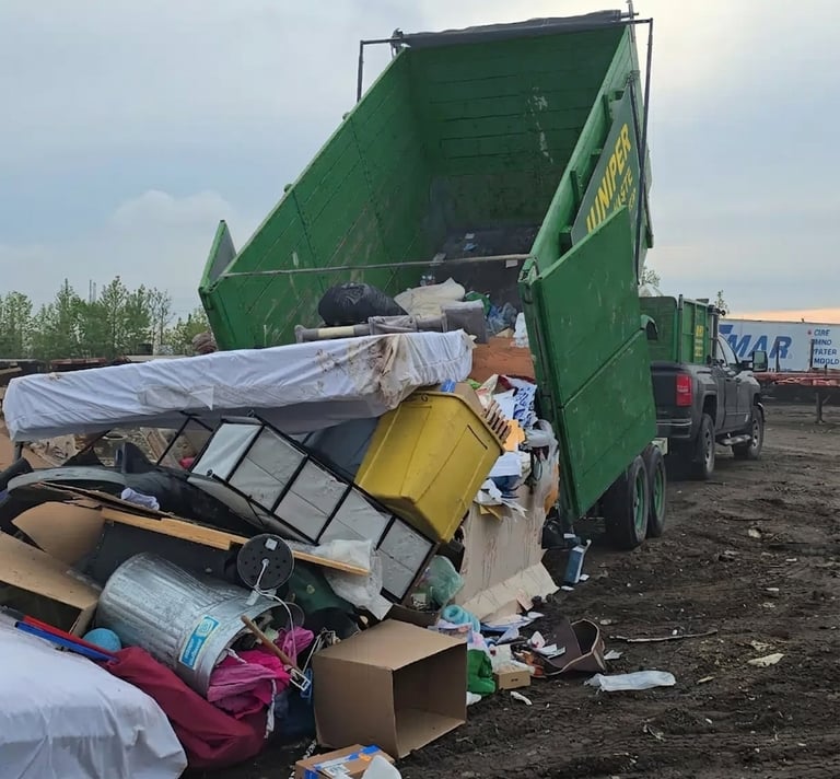 A green dumpster rental trailer unloading bulk junk, mattresses, and household waste at a landfill.