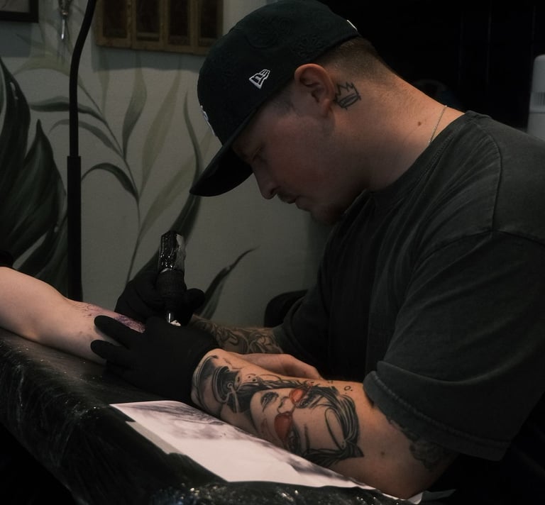 Professional tattoo artist with arm tattoos using a rotary machine to ink a client in a studio.