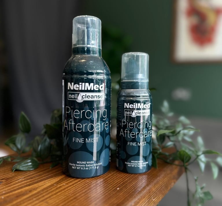 Two sizes of NeilMed Piercing Aftercare fine mist sterile saline solution spray on a wooden table.