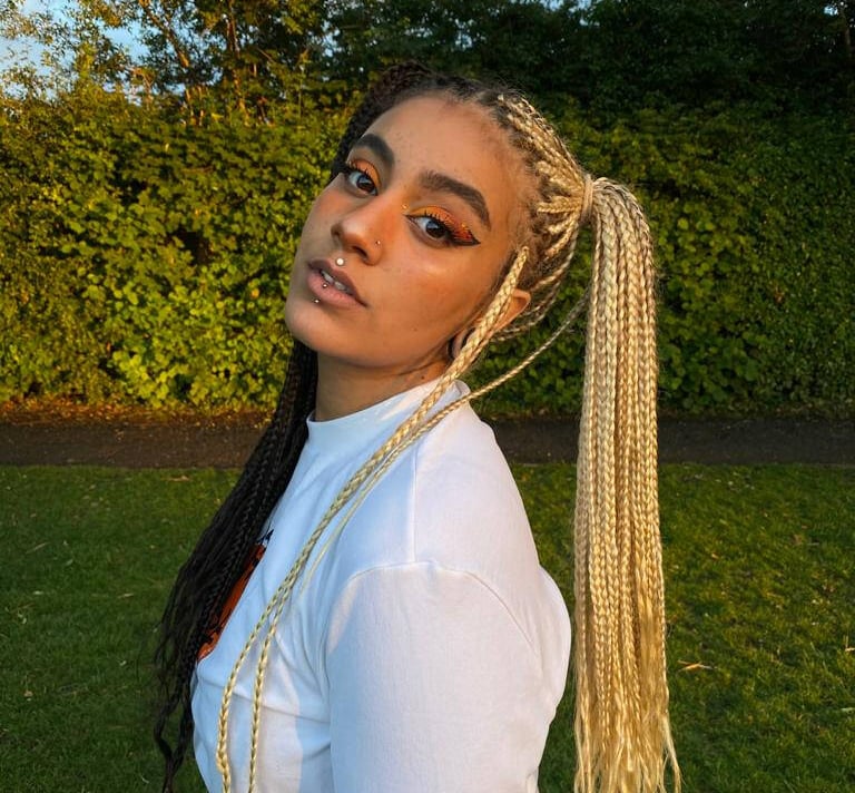 Woman with blonde and black split-dye box braids posing in a park at sunset.