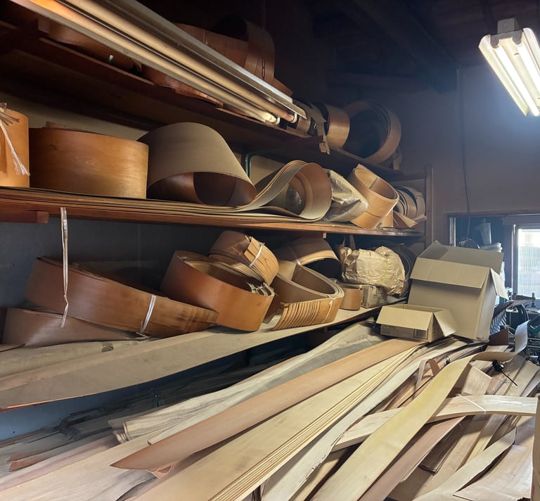 Curved wood veneer sheets and timber planks stored on shelves in a woodworking workshop.
