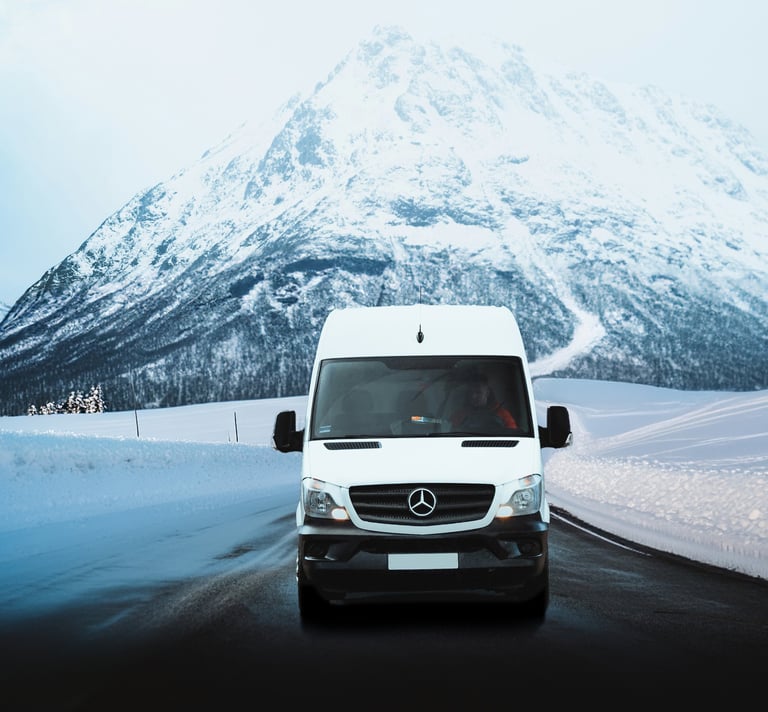 White Mercedes Sprinter van driving on a snowy mountain road in winter landscapes.