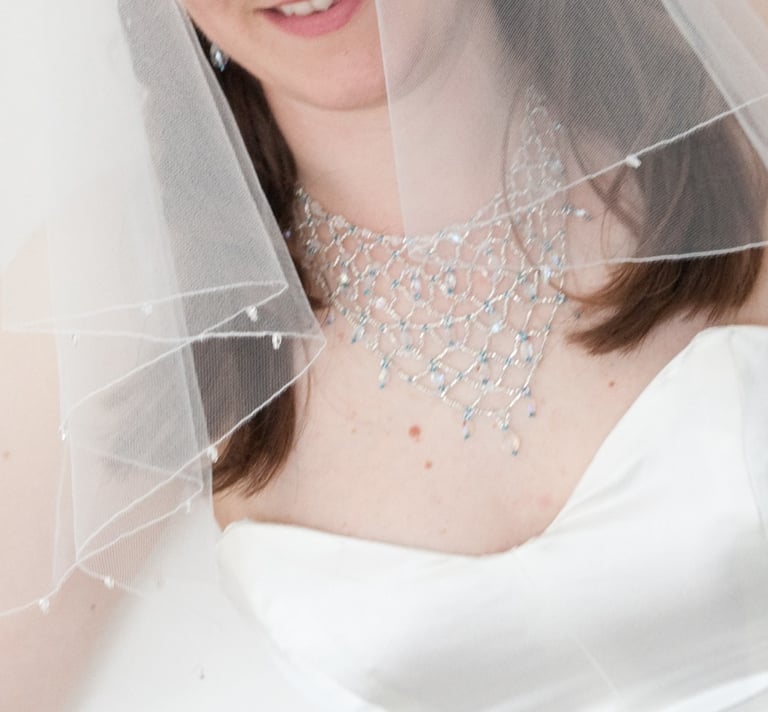 A bride wearing a white wedding dress and a sheer veil with a crystal bead bib necklace.