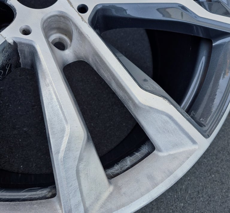 Close-up of a damaged alloy car wheel rim with visible curb rash and surface scratches.