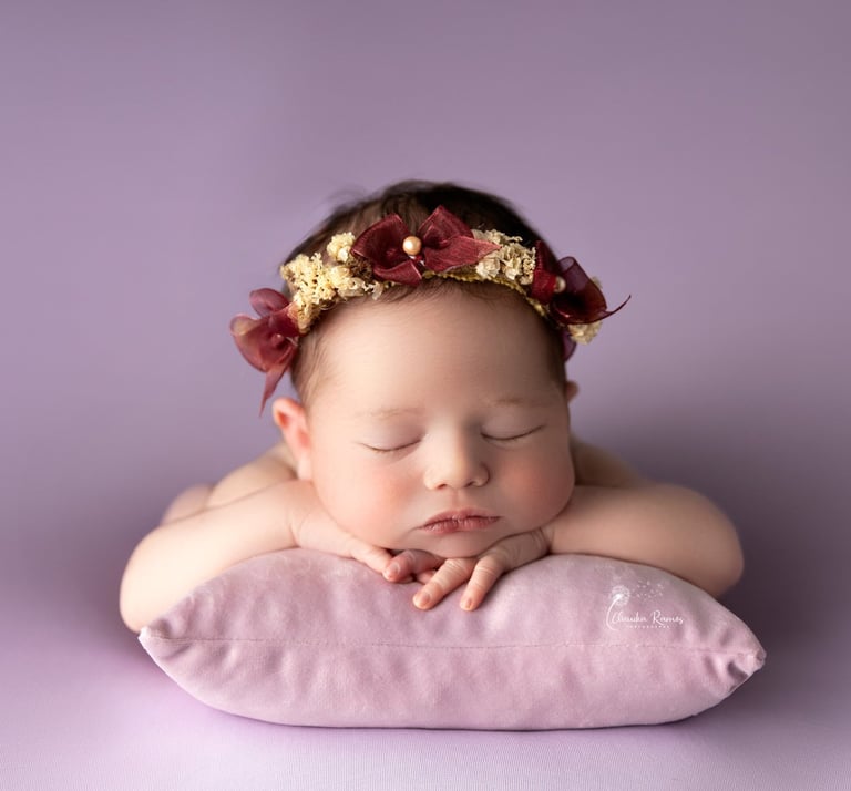 recién nacida con tocado dormida sobre almohada violeta