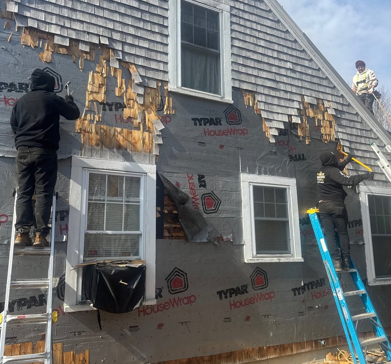 Professional contractors removing old cedar shingle siding from a house to install new exterior house wrap.