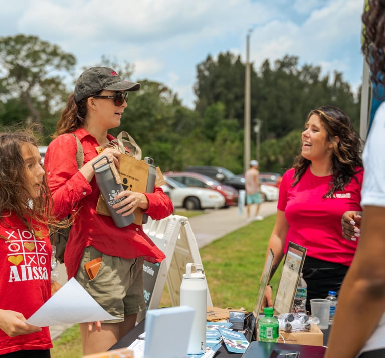 A lady wearing a red shirt with a little girl visiting an information booth