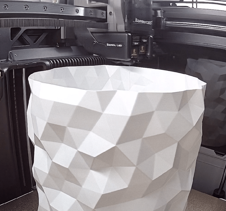 Bambu Lab 3D printer creating a white geometric low-poly vase with an industrial extruder.