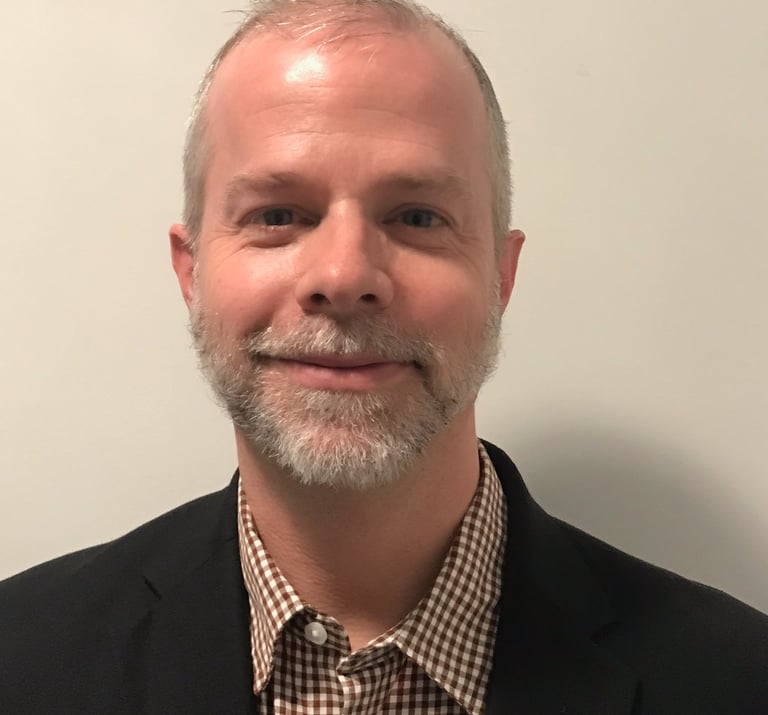 Alexander Slagg with grey beard, black sport coat, checkered button down shirt