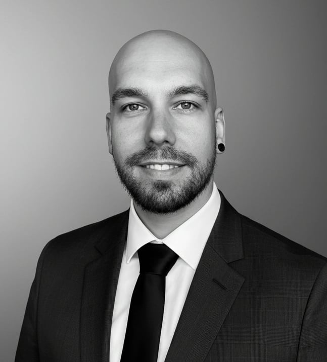 Professional black and white headshot of a bald man with a beard wearing a formal suit and tie.