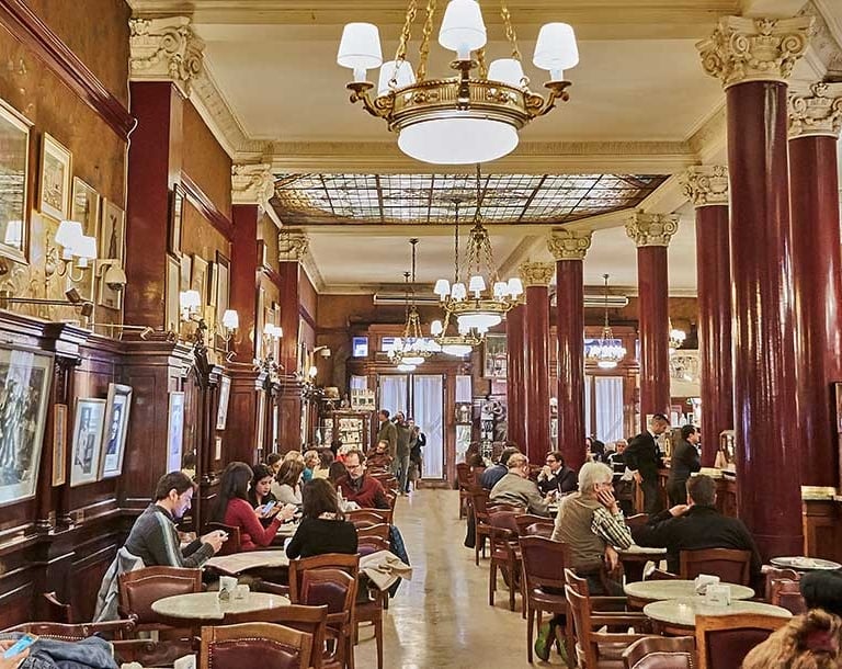 Historic European cafe interior with patrons at marble tables under ornate chandeliers and classic architecture.