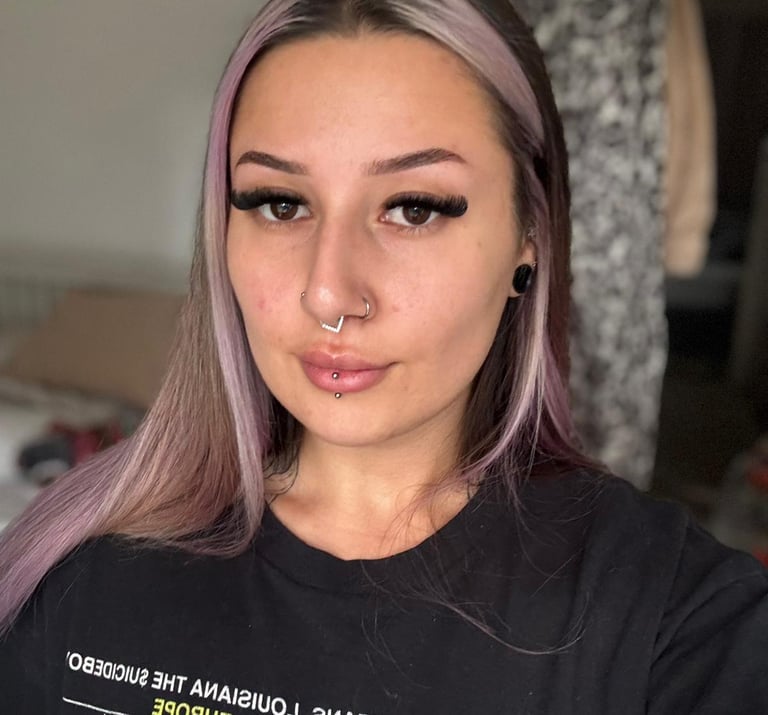 Woman with purple dyed hair and facial piercings wearing long volume eyelash extensions.