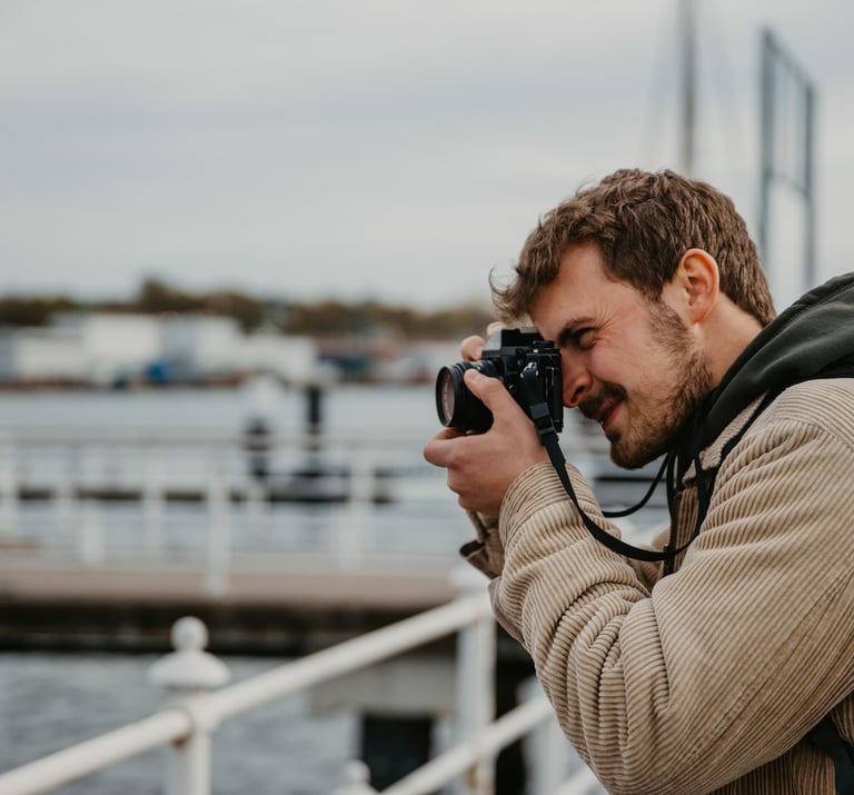 A male photographer taking a picture with a professional camera at a scenic waterfront harbor.