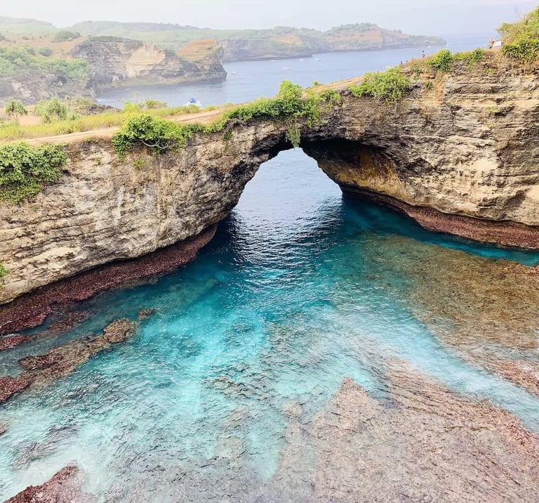 Natural rock arch at Broken Beach in Nusa Penida, Bali, over clear turquoise ocean water.