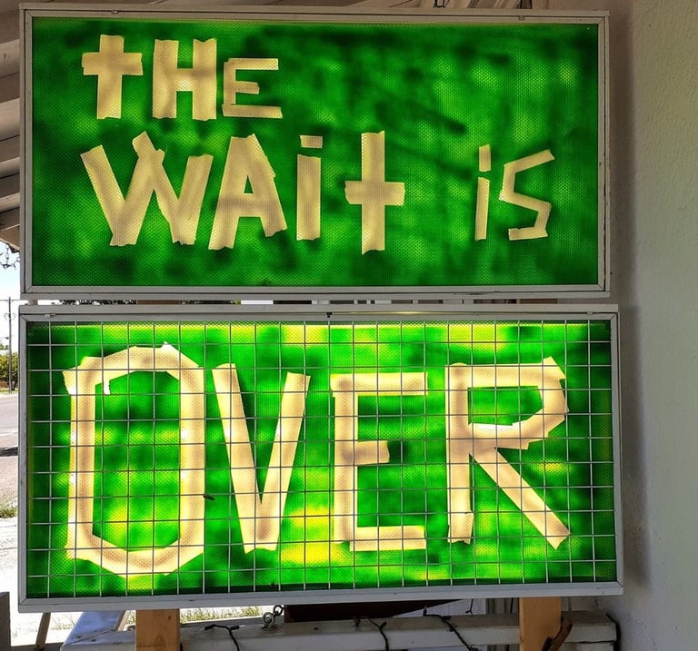 Illuminated green and yellow sign reading “The Wait Is Over.”